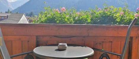 A round table with a chair, a small pot, and a wooden fence with flowers.
