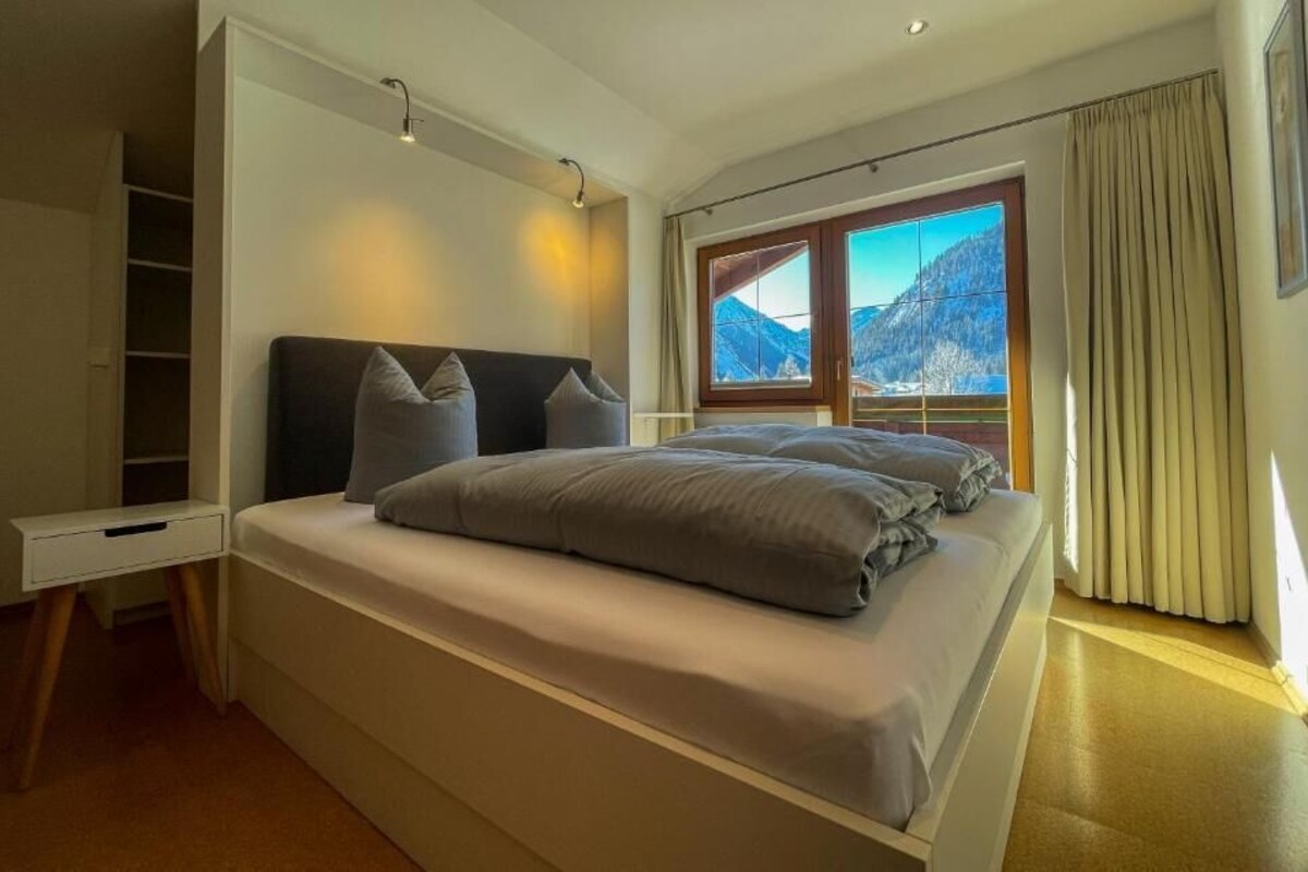 A bedroom with a bed, a bedside table, a wardrobe, and a window with a mountain view.