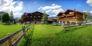 A wooden chalet-style building with a balcony, surrounded by a grassy field and mountains in the background. - Ferienwohnungen Tannheim - Martina Fügenschuh (Tannheim)