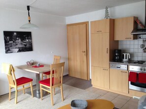 A compact kitchen with wooden cabinets, a dining table with red chairs, a hanging light fixture, and a coffee maker. - Ferienwohnungen Tannheim - Martina Fügenschuh (Tannheim)
