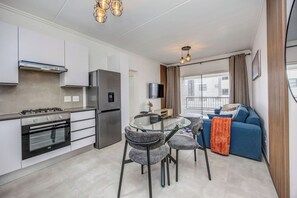 Eine moderne Küche mit Einbauofen, Kühlschrank und Essbereich mit Glastisch und Stühlen.