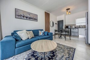 Een moderne woonkamer met een blauwe bank, een ronde houten salontafel en een kamerbreed tapijt met dessin.