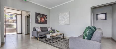 A modern living room with a grey sofa, a coffee table, and a rug. There is a painting on the wall and a window with a view.