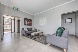 Ein modernes Wohnzimmer mit einem grauen Sofa, einem Couchtisch und einem Teppich. Ein Gemälde hängt an der Wand und ein Fenster bietet einen Ausblick.