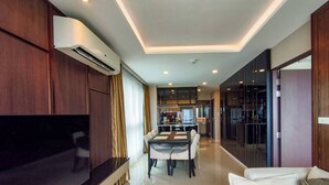 A modern living room with a flat-screen TV, a dining area with a table and chairs, and a kitchen in the background. - Luxurious 2BR Condo with Ocean Views in Choeng Thale (Tambon Choeng Thale)