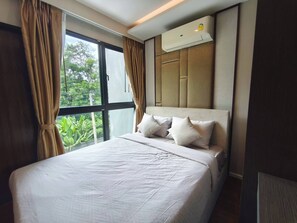 Ein Hotelzimmer mit einem großen Bett, einem Fenster mit Vorhängen, einer Klimaanlage und Blick auf Grünfläche.