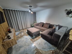 Una sala de estar con un sofá modular, un aparador de madera y un tapete estampado.