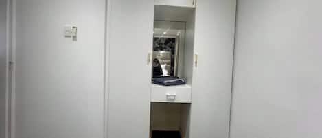 Un pasillo estrecho con una puerta de armario espejada, un mueble blanco pequeño y un suelo de baldosas negras.