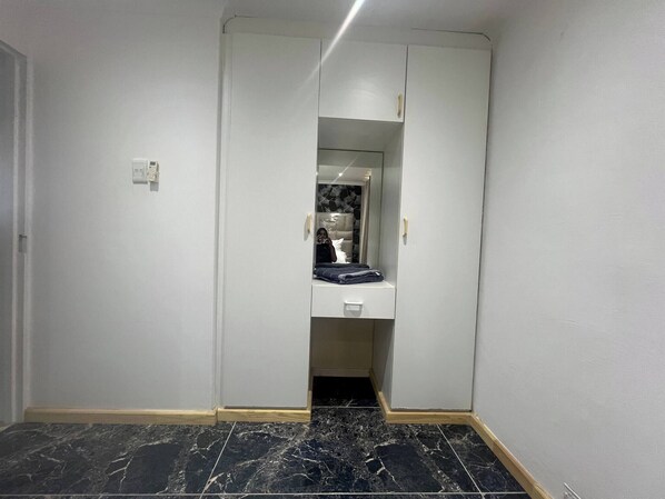 A narrow hallway with a mirrored closet door, a small white cabinet, and a black tiled floor.