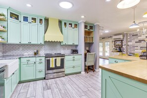 A kitchen with light green cabinets, a stainless steel oven, and a wooden countertop.