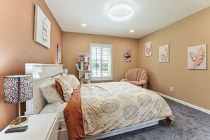 Ein Schlafzimmer mit Bett, Sessel, Schreibtisch, Lampe und Bildern an den Wänden.