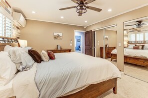 A bedroom with a large bed, a ceiling fan, a dresser, and a mirror.