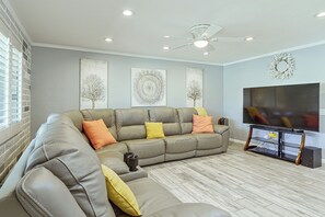 A living room with a sectional sofa, a flat-screen TV, decorative wall art, and a ceiling fan. - 7 Mi to Saguaro Nat’l Park! Mtn-View Haven w/ Pool (Tucson)
