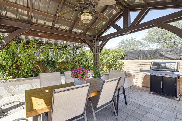An outdoor patio with a table, chairs, a grill, and a ceiling fan.