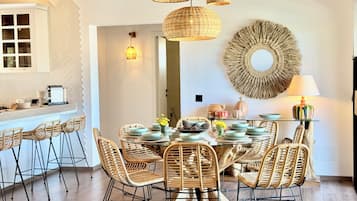 Un comedor con sillas de mimbre, una mesa redonda e iluminación colgante de mimbre.