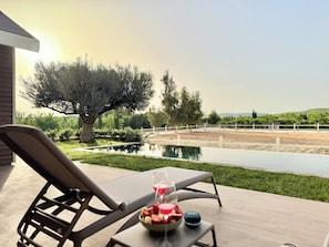 Un patio con una mesa preparada para una comida, una piscina y vistas a un área cercada con árboles y colinas.