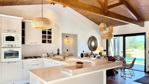 A modern kitchen with white cabinetry, a central island, and a dining area with a view. - Kenz Essia Luxury countryside escape near Tunis (Chaouat)