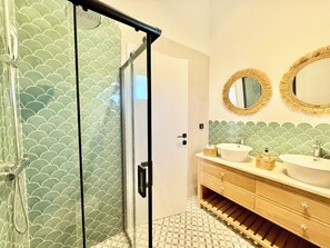 Casa de banho com cabine de duche em vidro, duas lavatórios com espelhos redondos e chão em mosaico.