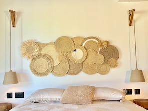 A bed with a large woven wall hanging, two pendant lights, and a fluffy throw pillow.