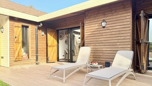A modern outdoor patio with two lounge chairs and a small table, wooden exterior walls, and a sliding glass door leading to an interior space. - Kenz Essia Luxury countryside escape near Tunis (Chaouat)