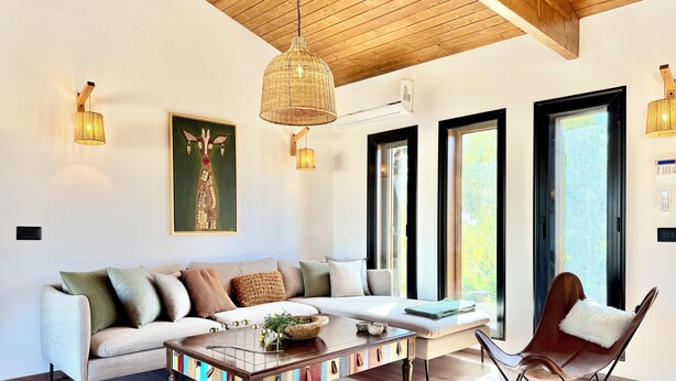 A modern living room with a sofa, coffee table, and a chair. There are large windows and a ceiling with wooden beams. - Kenz Essia Luxury countryside escape near Tunis (Chaouat)