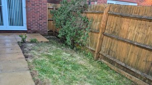 A residential backyard with a brick wall, a wooden fence, and a concrete pathway. - Elegant Guest Room Retreat in West Midlands (West Midlands)