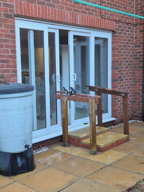 A brick building with a white-framed sliding glass door, a wooden bench, and a black trash bin.