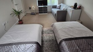A room with two beds, a sofa, a small table, a TV, a plant, and a window with blinds. - Elegant Guest Room Retreat in West Midlands (West Midlands)