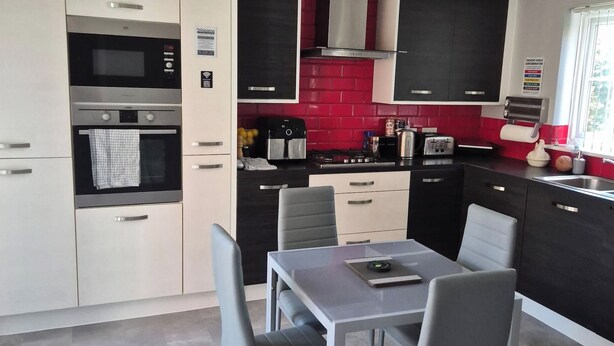 A modern kitchen with built-in appliances, a dining area with a table and chairs, and a red-tiled backsplash. - Elegant Guest Room Retreat in West Midlands (West Midlands)