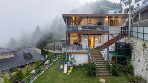 Un bâtiment à deux étages doté d’un balcon, d’un escalier et d’un jardin avec une balançoire.