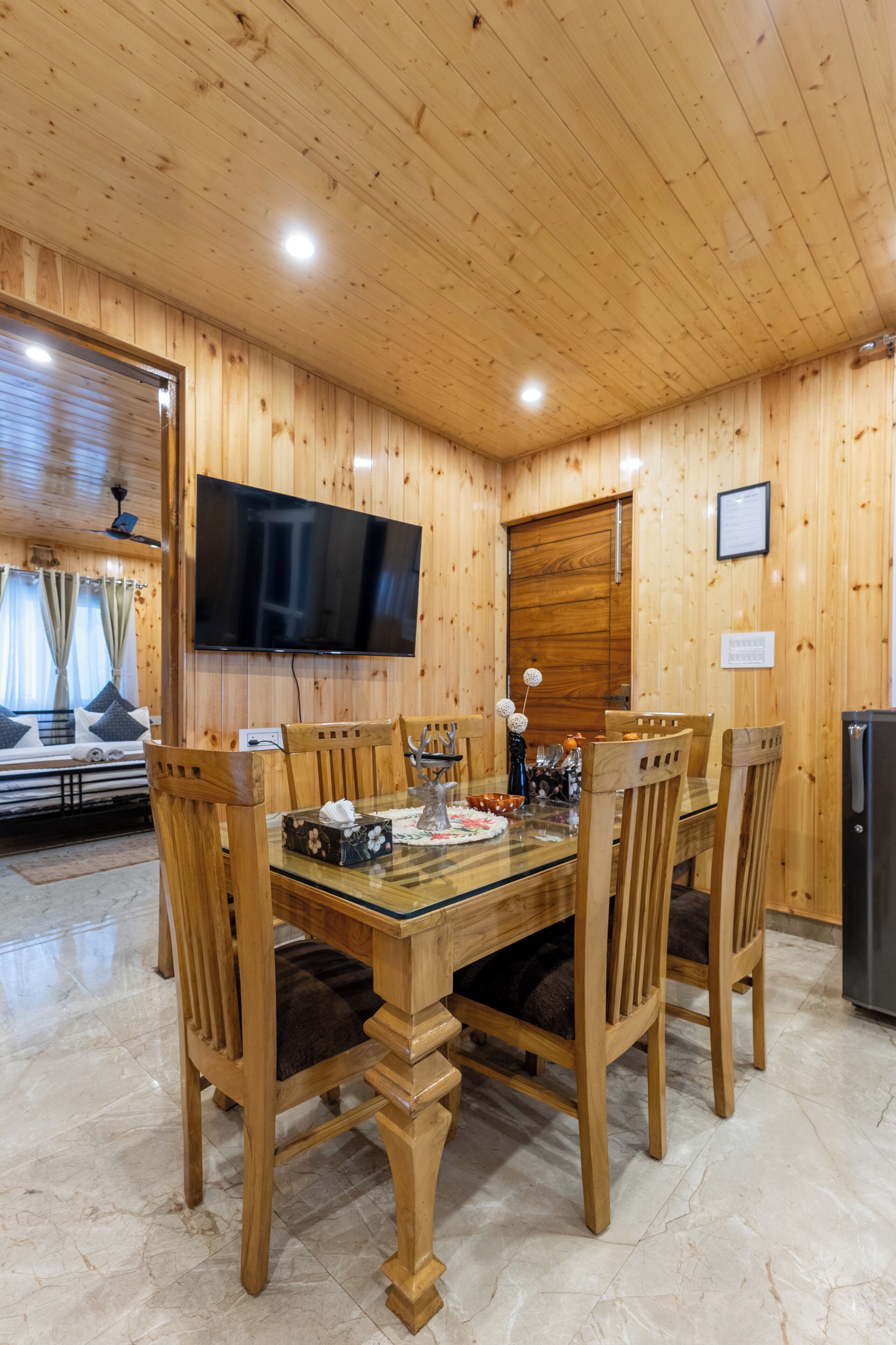 Habitación con paneles de madera, una mesa de comedor, sillas, un televisor de pantalla plana y una cama con cortinas.
