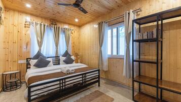 Un dormitorio con paneles de madera, una cama, un ventilador de techo, una ventana con cortinas y una estantería.