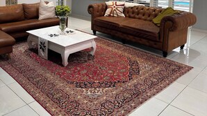 Una sala de estar con un sofá de cuero marrón, una mesa de centro blanca y una alfombra estampada.