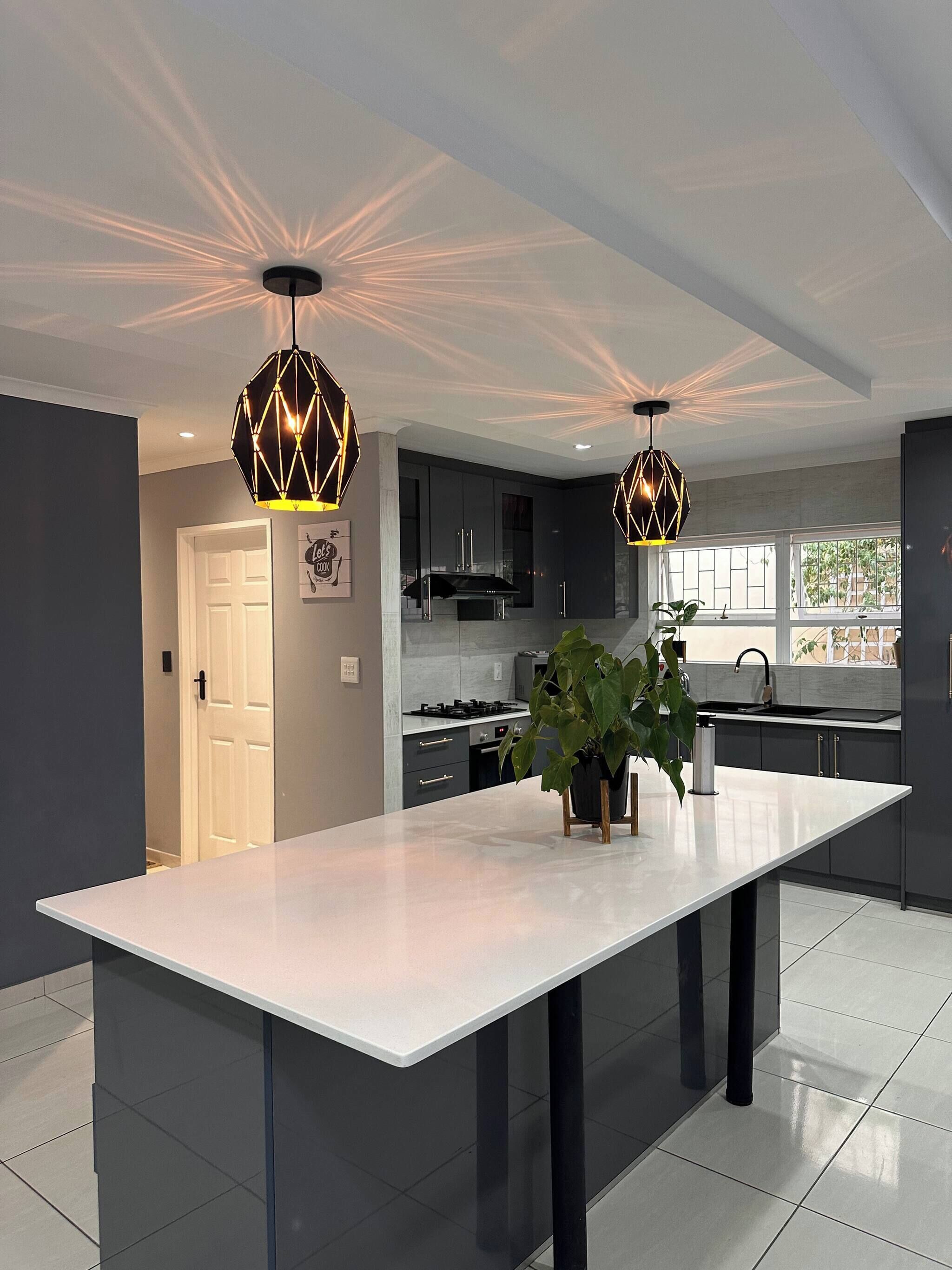 Una cocina moderna con una isla central, luces colgantes y vistas al exterior.