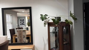 Una sala de estar moderna con comedor, un espejo grande, un aparador de madera y una planta en maceta.