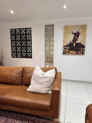 A brown leather sofa with a white pillow, a patterned rug, a decorative wall panel, and a painting. - Entertainers delight near the beach & wine routes! (Cape Town)