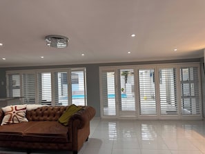 A spacious living room with a brown leather sofa, white tiled floor, and large glass doors with white blinds. - Entertainers delight near the beach & wine routes! (Cape Town)