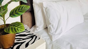 Una cama con cabecera, ropa de cama blanca y una planta en maceta.