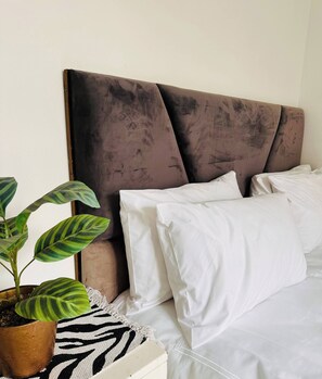 Ein Bett mit Kopfteil, weißer Bettwäsche und einem Blumentopf.