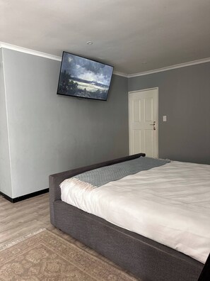 A bedroom with a bed, a television mounted on the wall, and a door. - Entertainers delight near the beach & wine routes! (Cape Town)