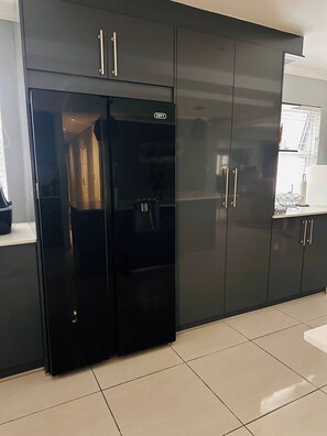 A modern kitchen with dark cabinetry, a built-in refrigerator, and a countertop with a kettle. - Entertainers delight near the beach & wine routes! (Cape Town)