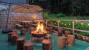 Un patio al aire libre con un brasero, taburetes de madera y luces colgantes.