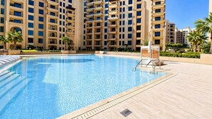 A swimming pool with a clear blue water surface, surrounded by a tiled deck and palm trees. - Jadeel Residences- MJL - Dubai (Dubai)
