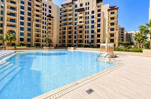 A swimming pool with a clear blue water surface, surrounded by a tiled deck and palm trees. - Jadeel Residences- MJL - Dubai (Dubai)