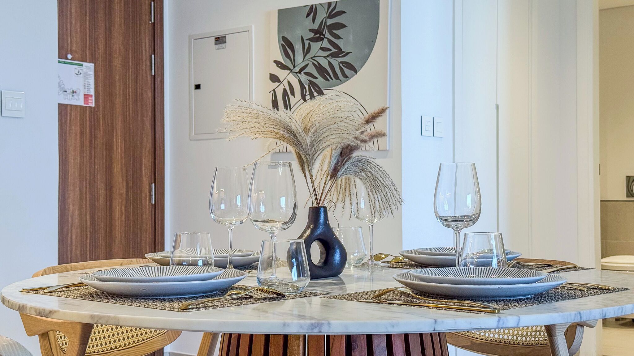 Une table ronde, dressée pour le repas, avec des assiettes, des couverts et des verres à vin.