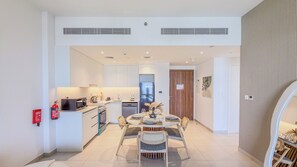 A modern kitchen with a dining area, including a table set for four, a refrigerator, and a microwave. - Jadeel Residences- MJL - Dubai (Dubai)