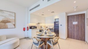A modern kitchen with white cabinets, a central island, and a dining area with a round table and chairs. - Jadeel Residences- MJL - Dubai (Dubai)