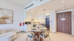 A modern kitchen with white cabinets, a central island, and a dining area with a round table and chairs. - Jadeel Residences- MJL - Dubai (Dubai)