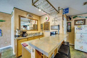 A kitchen with a large island, a bar sign, a pay phone, and a refrigerator with magnets.