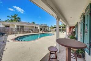 A swimming pool with a patio area, a covered seating area, and a view of a residential building in the background.